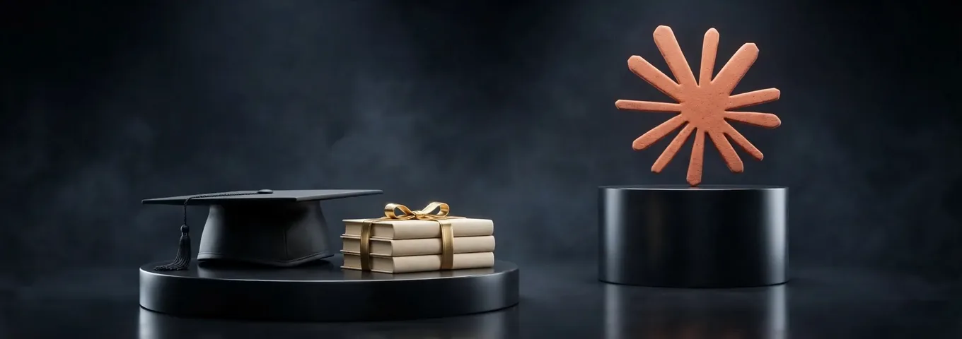 A black graduation cap and a stack of cream books tied with a gold ribbon on a low black plinth, beside a terracotta Claude starburst on a taller black plinth in a dark studio.